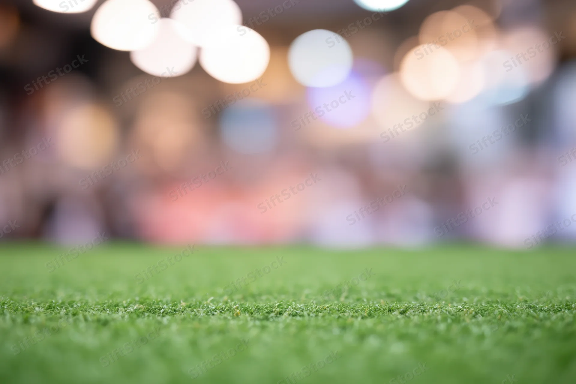 Close-up of green grass field with blurred stadium lights and crowd in background