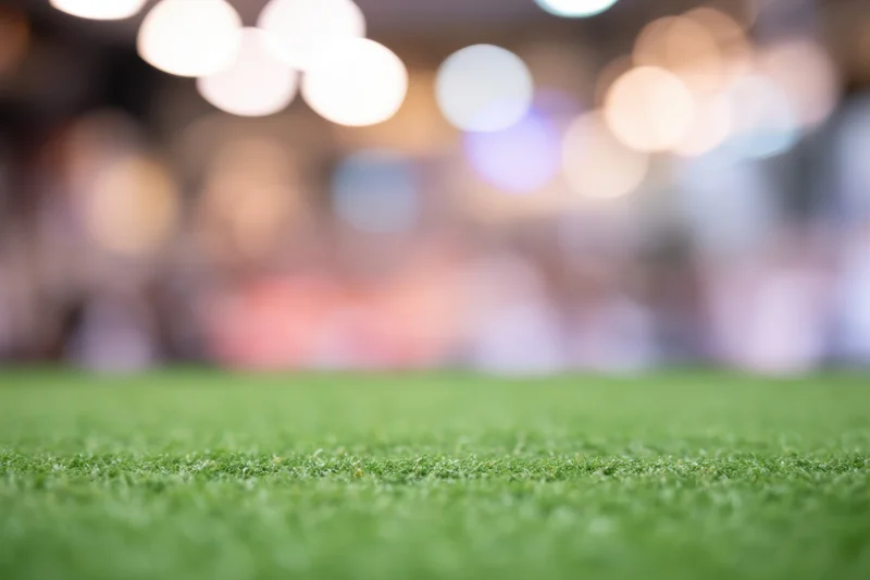 Close-up of green grass field with blurred stadium lights and crowd in background