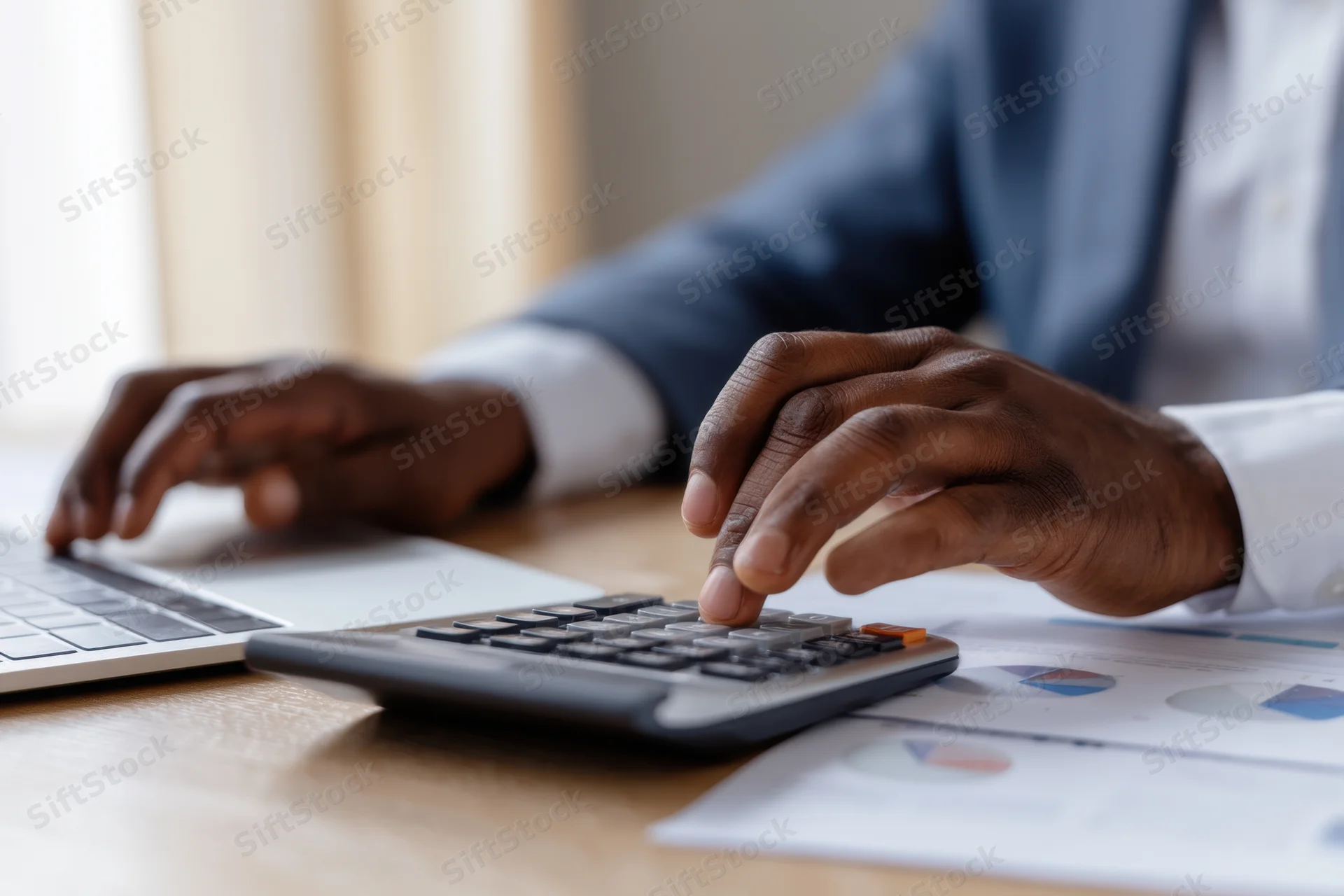 Man using calculator and laptop at office desk with financial documents