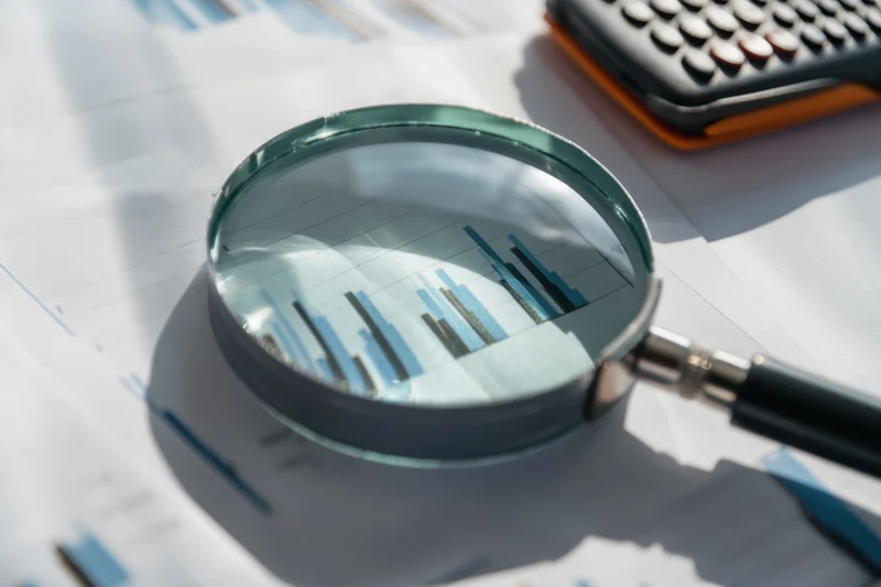 Magnifying glass over financial charts on office desk with calculator nearby