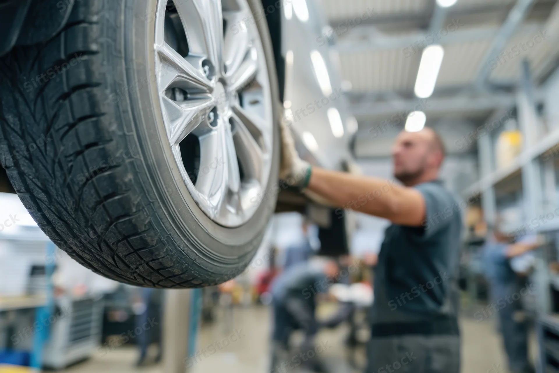 Close-up of a car tire mounted on an alloy wheel being inspected by a mechanic in an automotive workshop