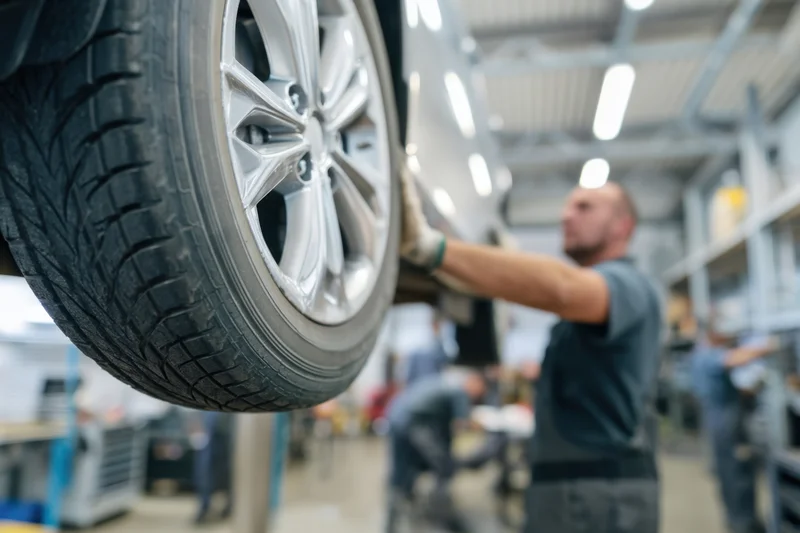 Close-up of a car tire mounted on an alloy wheel being inspected by a mechanic in an automotive workshop