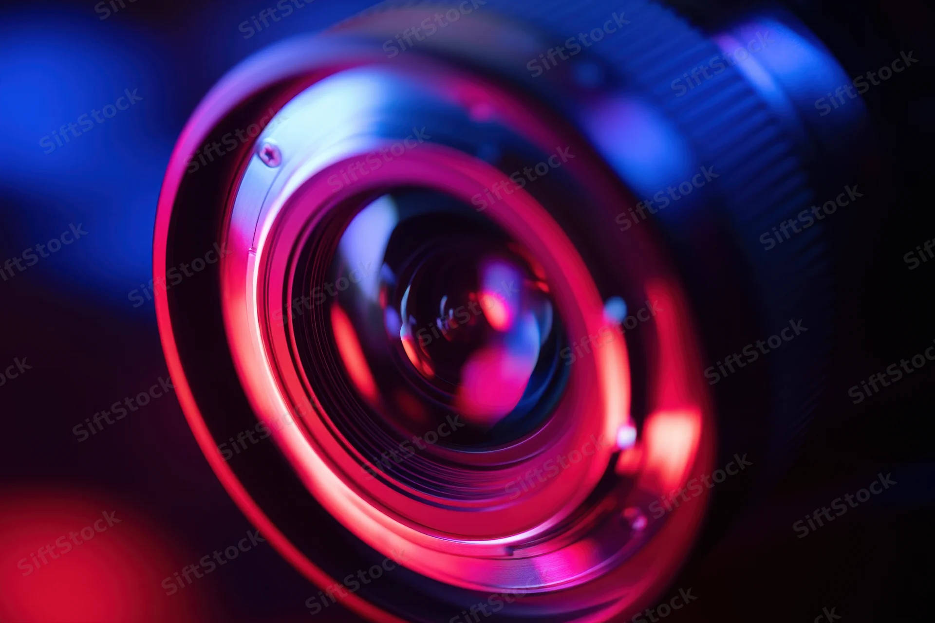Close-up of a camera lens with red and blue light reflections on glass surface