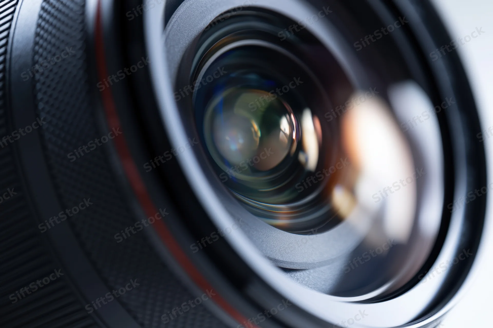 Closeup of a camera lens showing glass elements and reflective surfaces with a textured grip and red accent ring