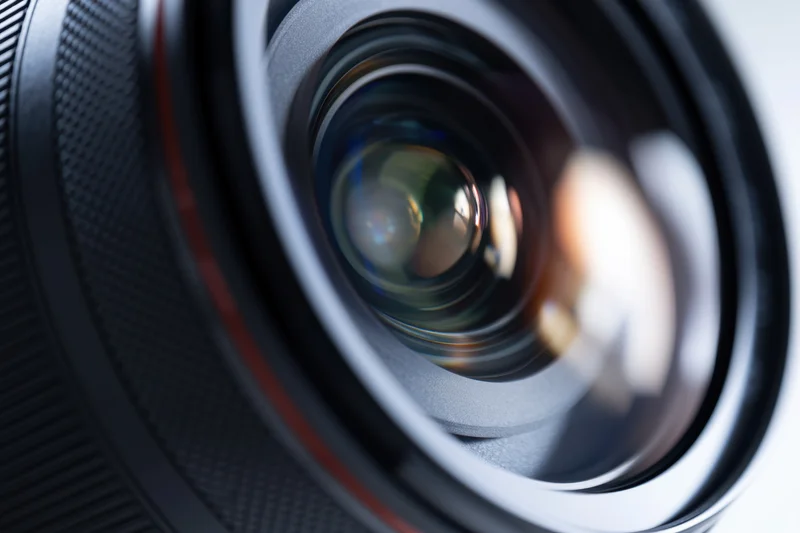 Closeup of a camera lens showing glass elements and reflective surfaces with a textured grip and red accent ring