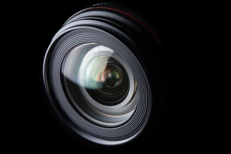 Close-up of a camera lens showing its glass elements and aperture rings against a black background