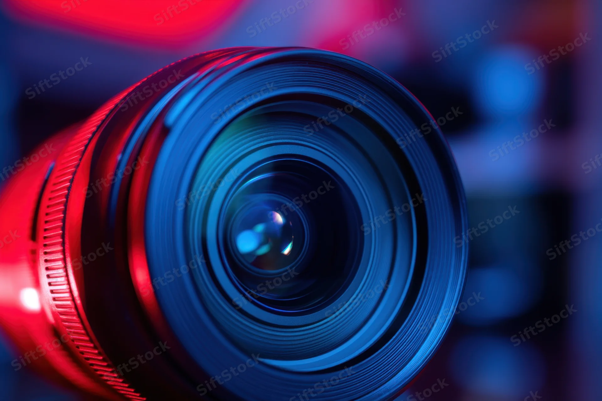 Closeup of a camera lens with blue and red neon lighting highlighting its glass and aperture structure