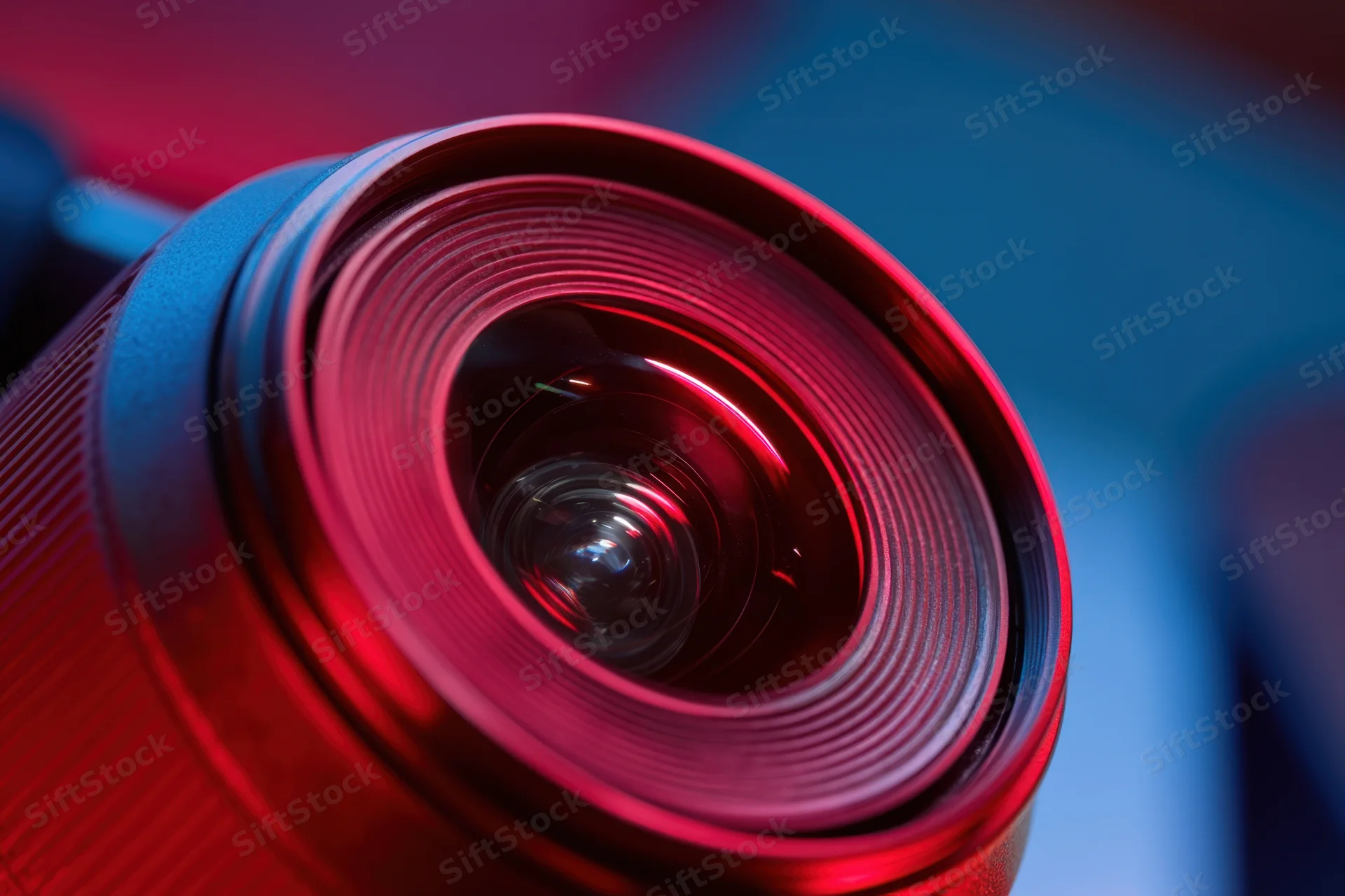 Closeup of a camera lens showing its glass elements and reflective surface under red and blue lighting