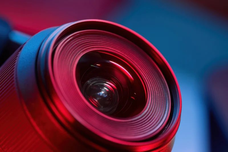 Closeup of a camera lens showing its glass elements and reflective surface under red and blue lighting