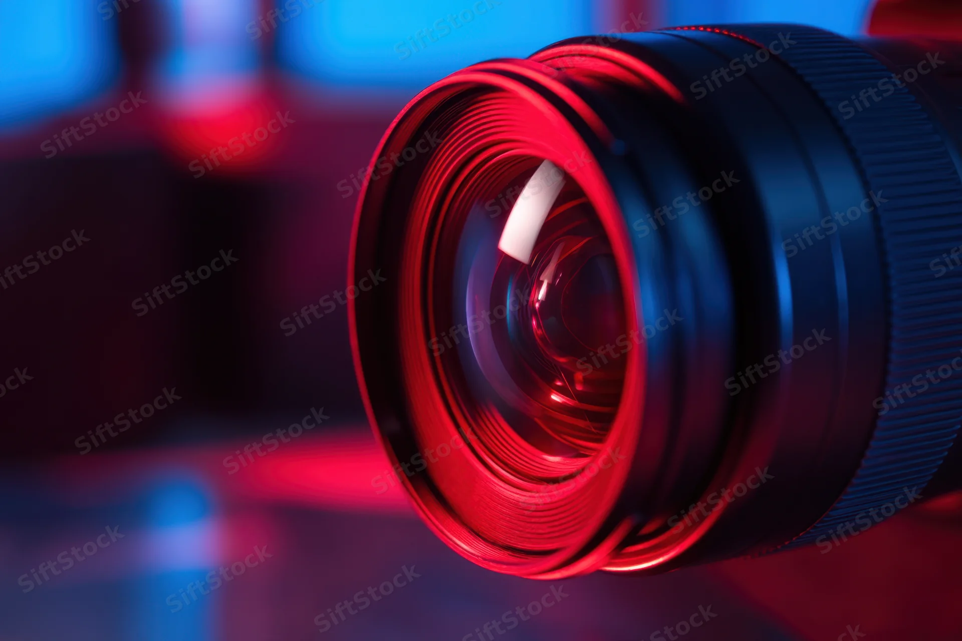 Closeup of a camera lens with red and blue neon lighting reflecting on its glass surface