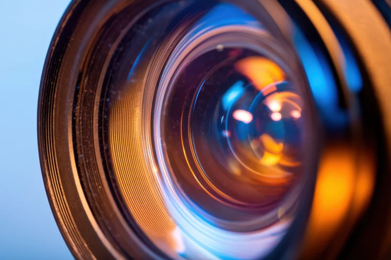 Closeup of a camera lens showing internal glass elements and colorful reflections