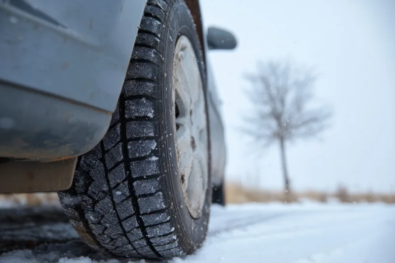Closeup of a car tire on a snowy road with visible tread and frost in a winter landscape