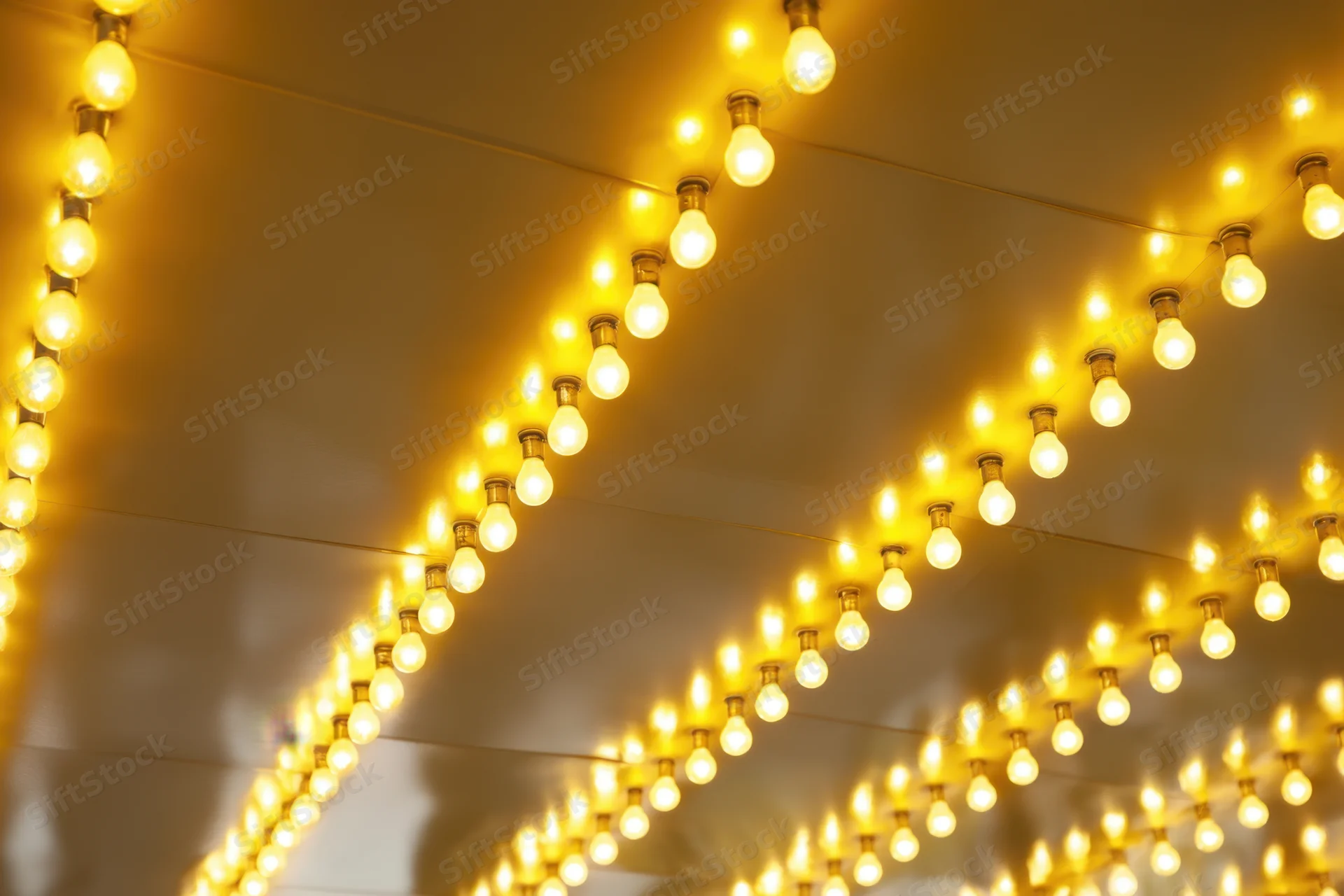 Rows of warm yellow bulbs arranged in parallel lines on a ceiling for decorative lighting