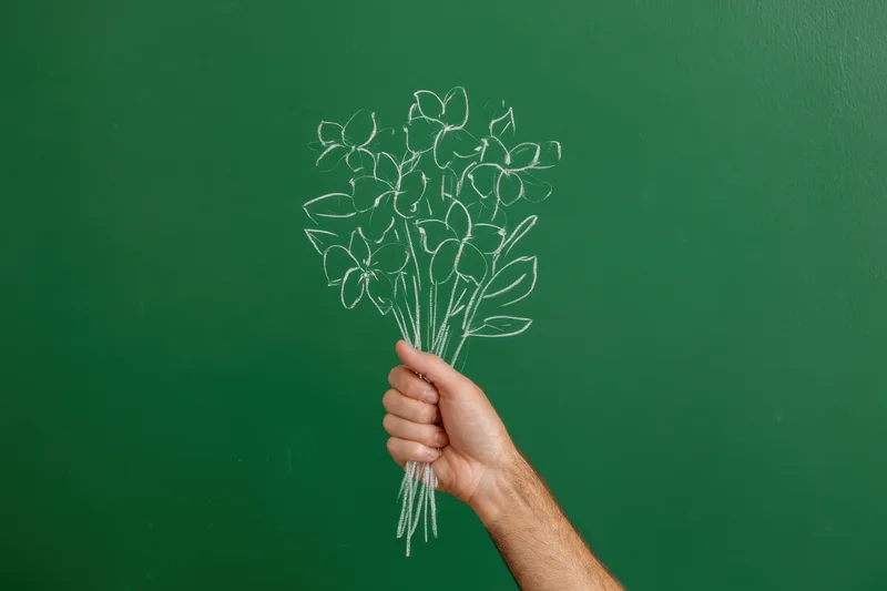 Hand holding a chalk-drawn bouquet of flowers on a green chalkboard