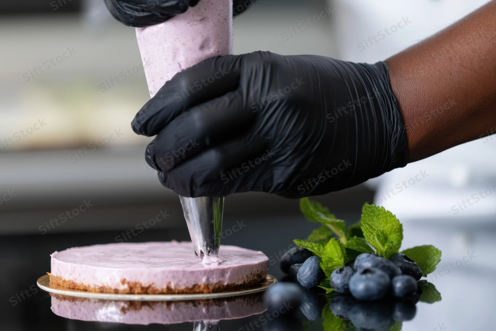 Chef in black gloves piping lavender frosting onto a blueberry cake in a kitchen setting