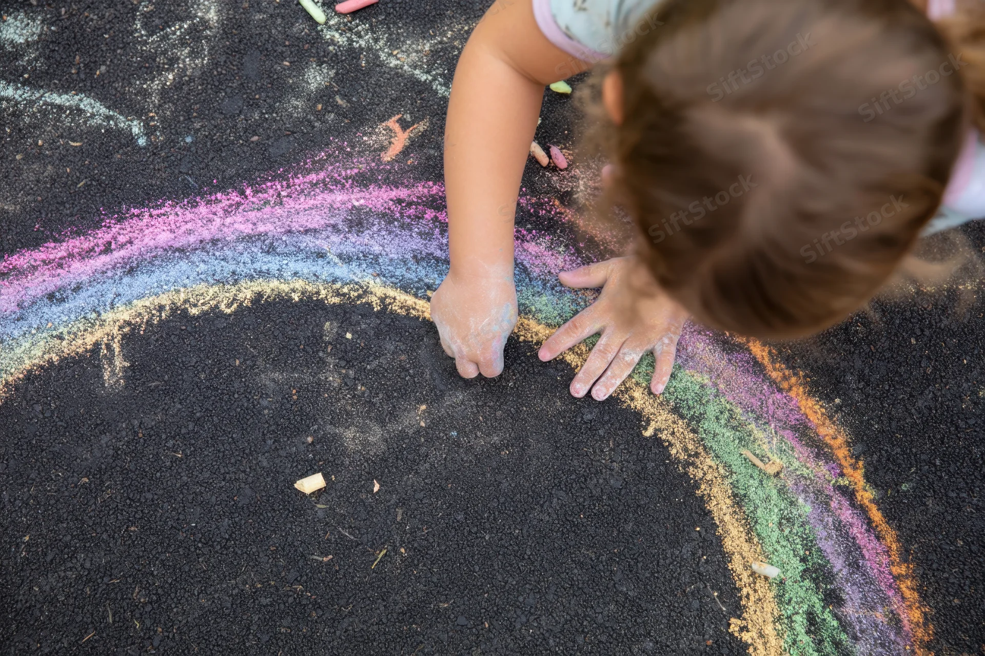 Child drawing a rainbow with colorful chalk on black pavement
