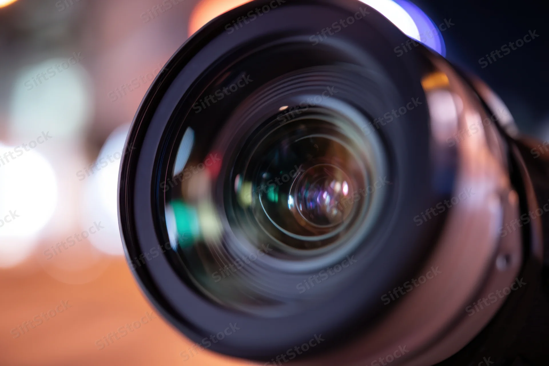 Close-up of a camera lens with multi-colored reflections and blurred background lights