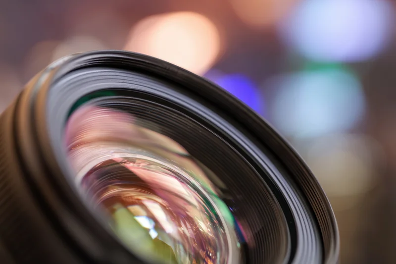 Close-up of a camera lens showing multi-colored reflections with blurred bokeh background