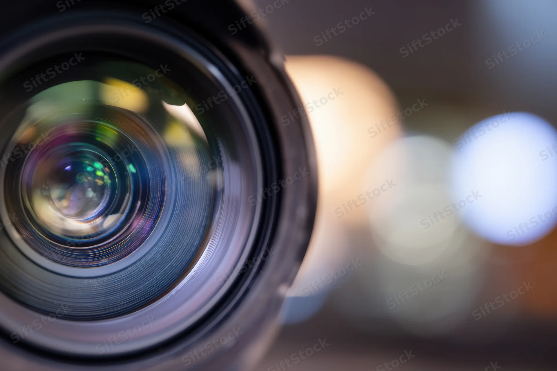 Close-up of a camera lens with multi-colored reflections and blurred bokeh lights in the background