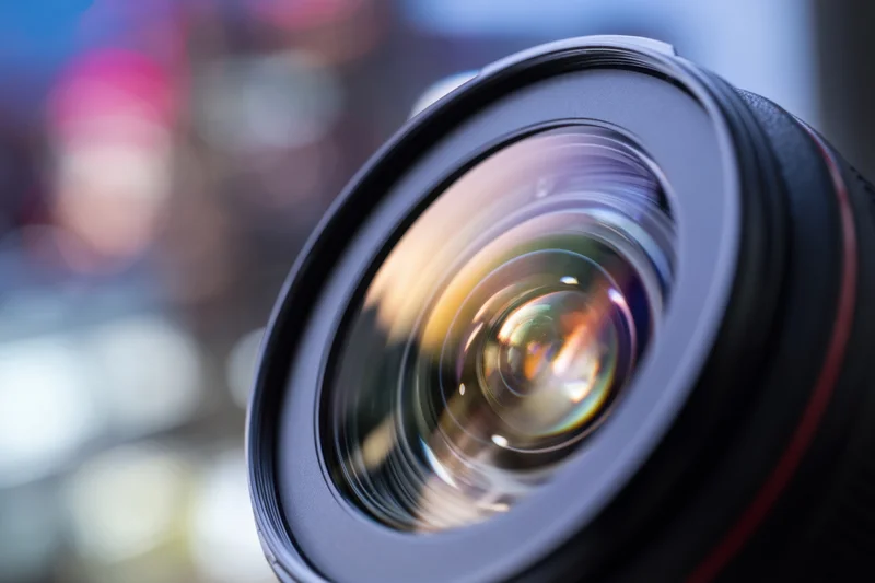 Close-up of a camera lens with multi-colored reflections and blurred background