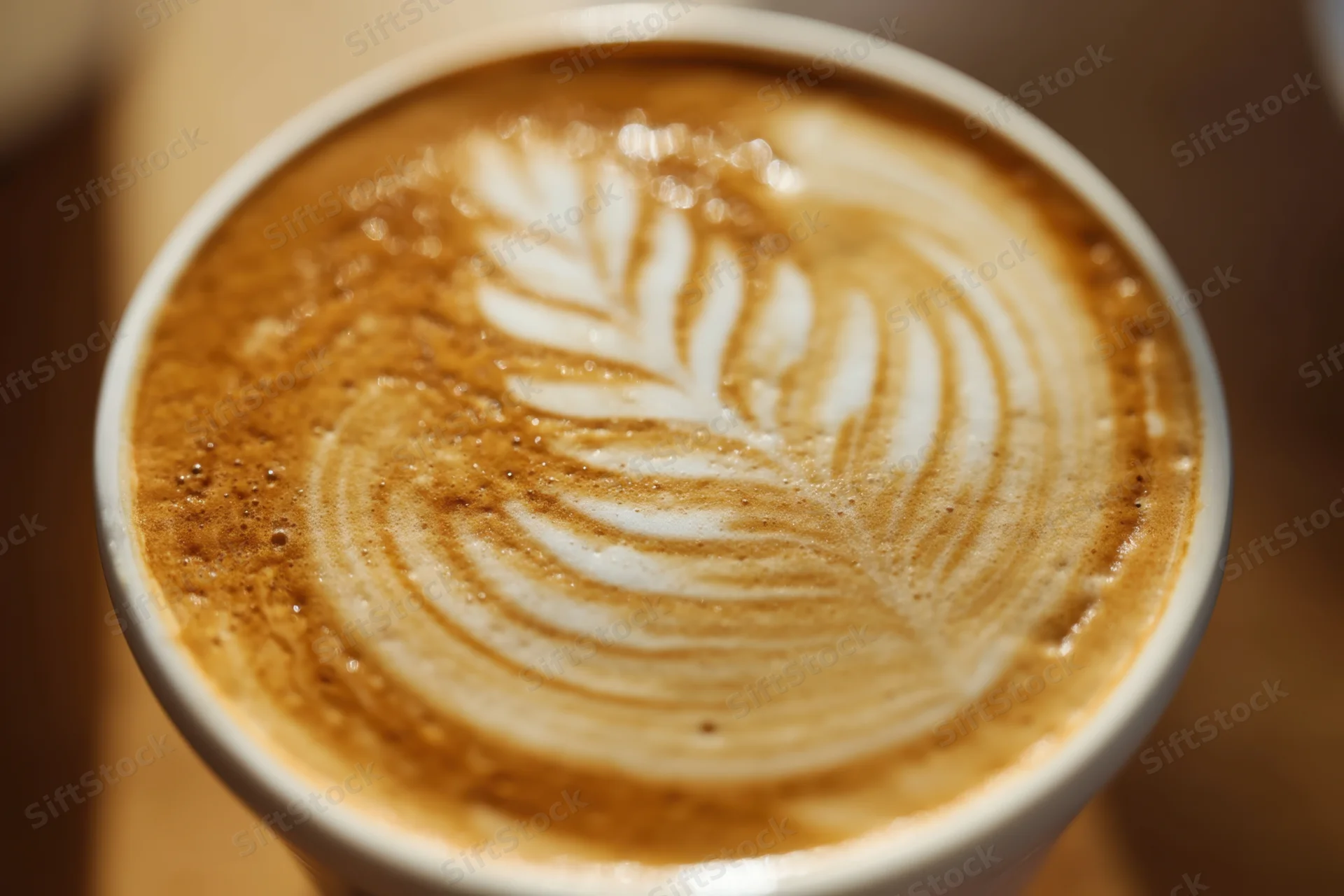 Close-up of latte art with leaf pattern in a white cup on wooden surface