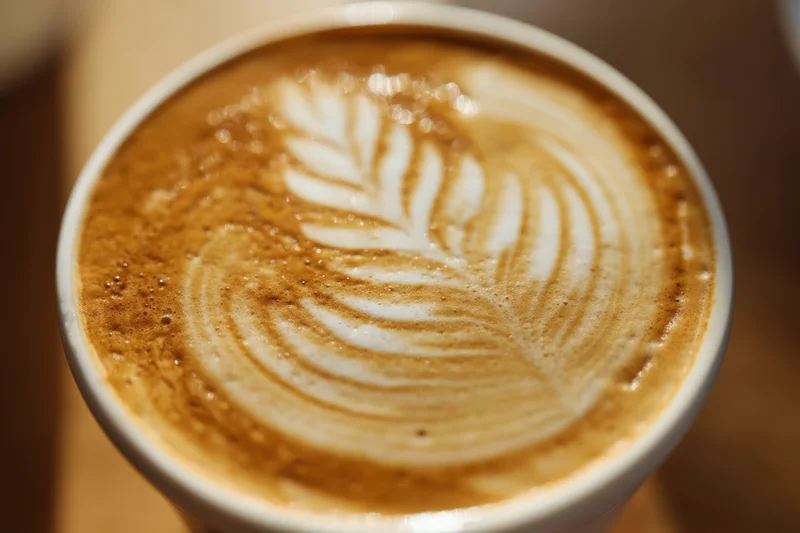 Close-up of latte art with leaf pattern in a white cup on wooden surface