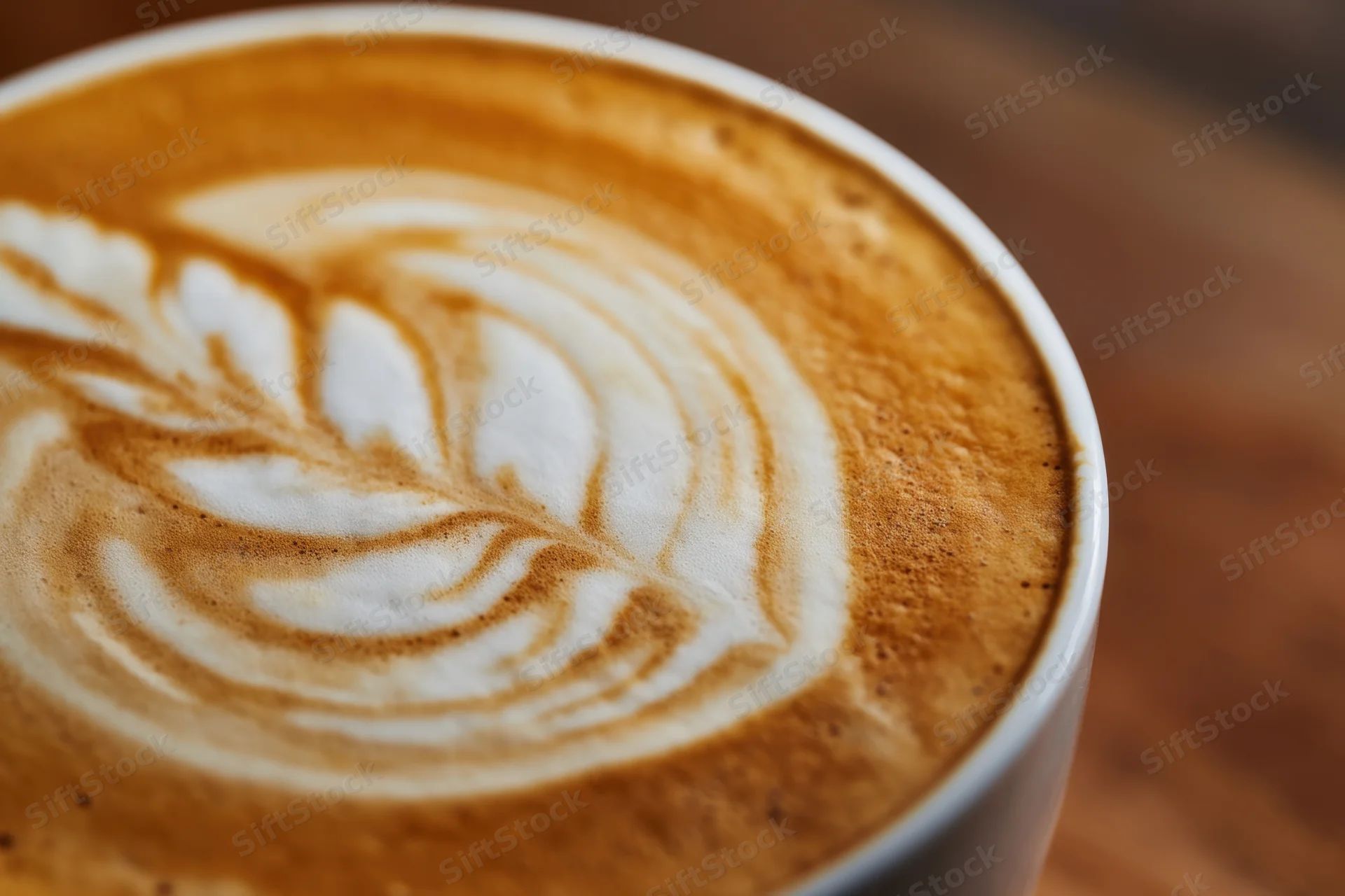 Close-up of latte art with leaf pattern in coffee foam on wooden table