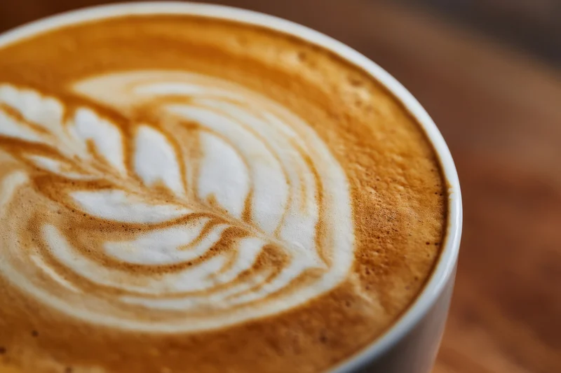 Close-up of latte art with leaf pattern in coffee foam on wooden table