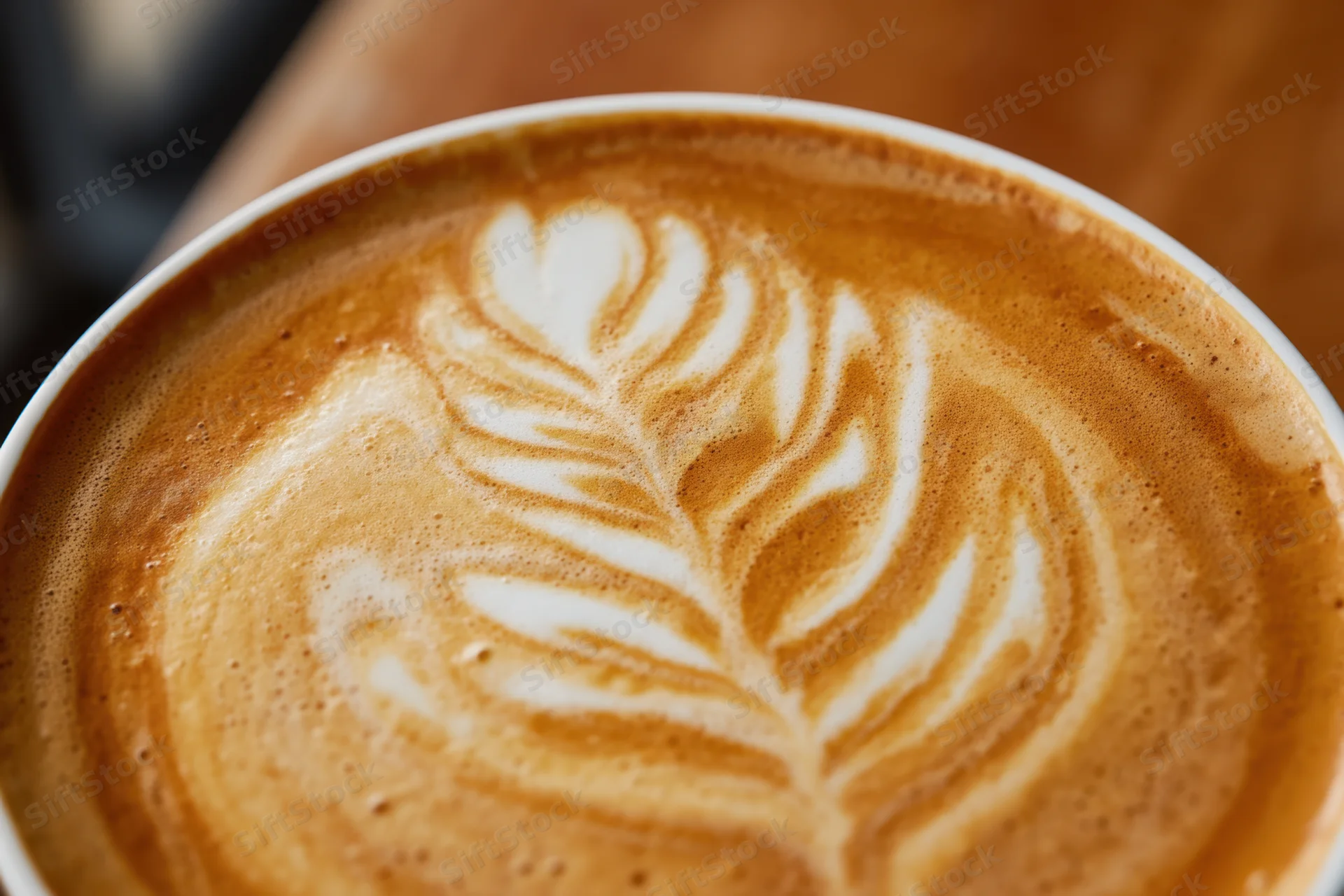 Close-up of latte art featuring a detailed leaf pattern in coffee foam on a cup surface