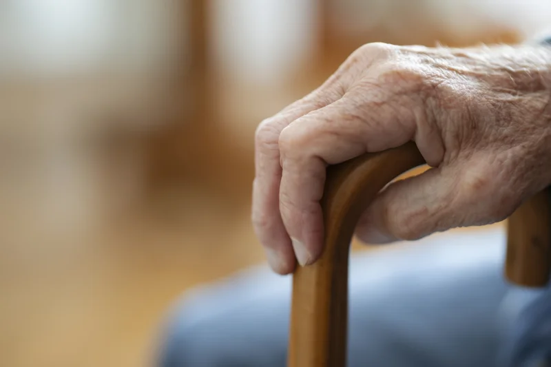 Close-up of an elderly hand gripping a wooden cane for support indoors