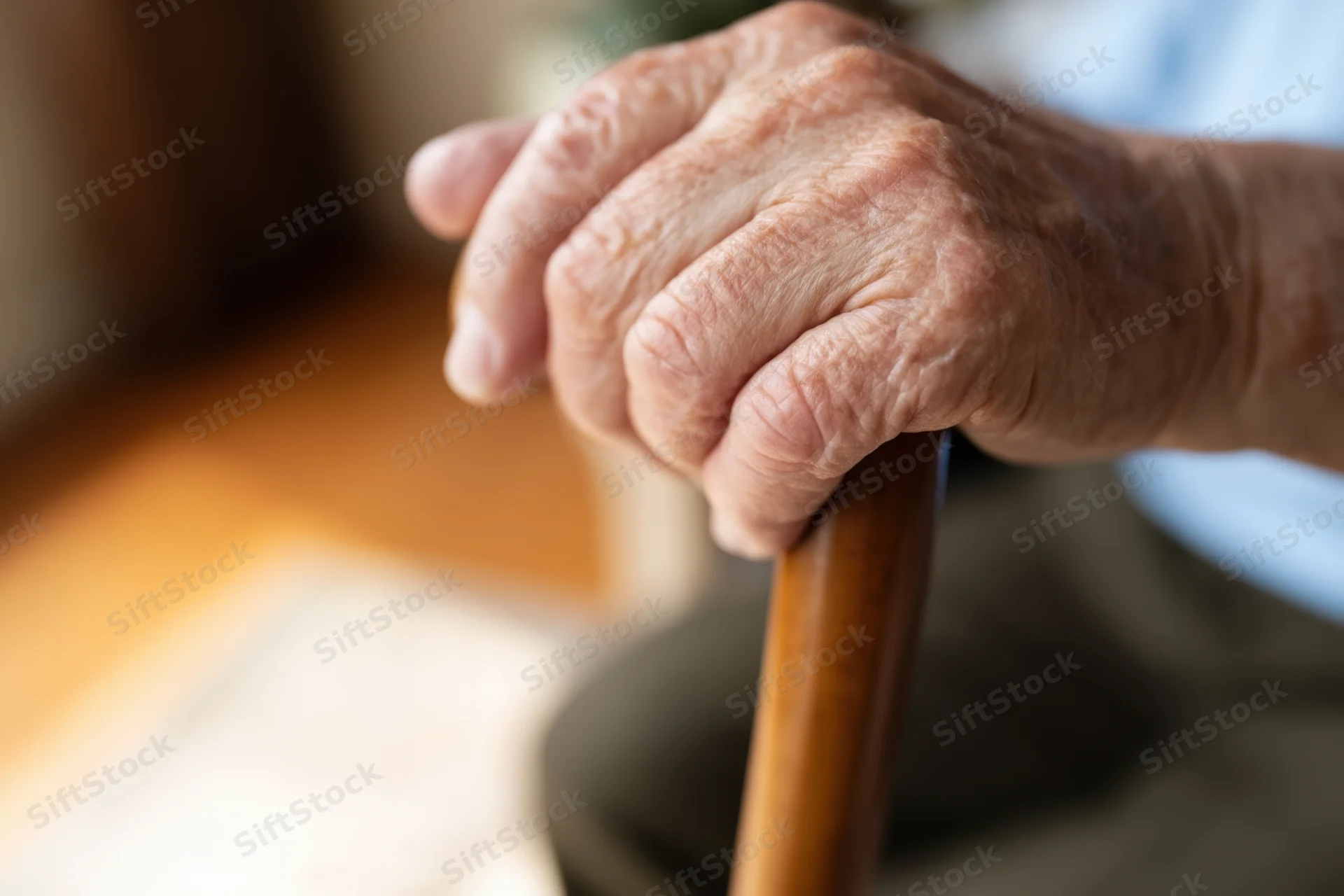 Close-up of an elderly hand gripping a wooden cane for support