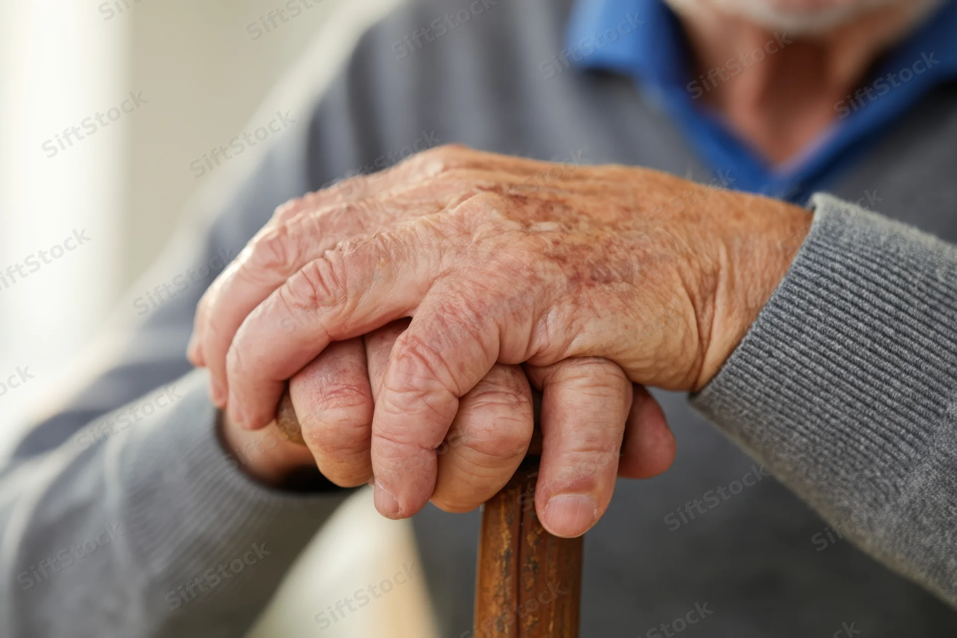 Close-up of an elderly man's hands gripping a wooden cane for support