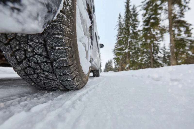 Close-up of a car tire gripping a snow-covered road in a winter forest setting