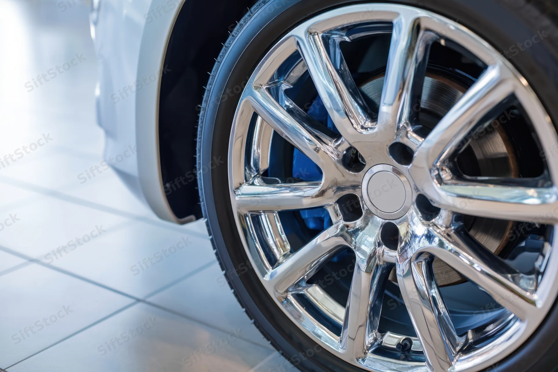 Close-up of a chrome alloy wheel on a white car in a showroom setting