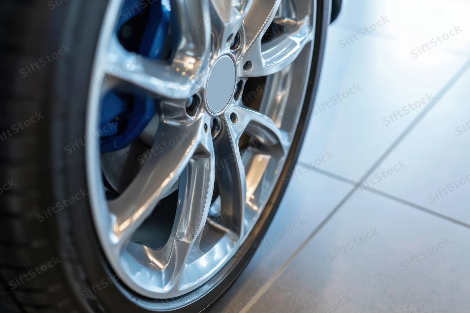Close-up of a car wheel with silver alloy rim and blue brake caliper on a glossy tiled floor