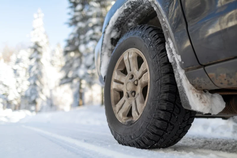Close-up of black suv tire on snowy road surrounded by snow-covered trees