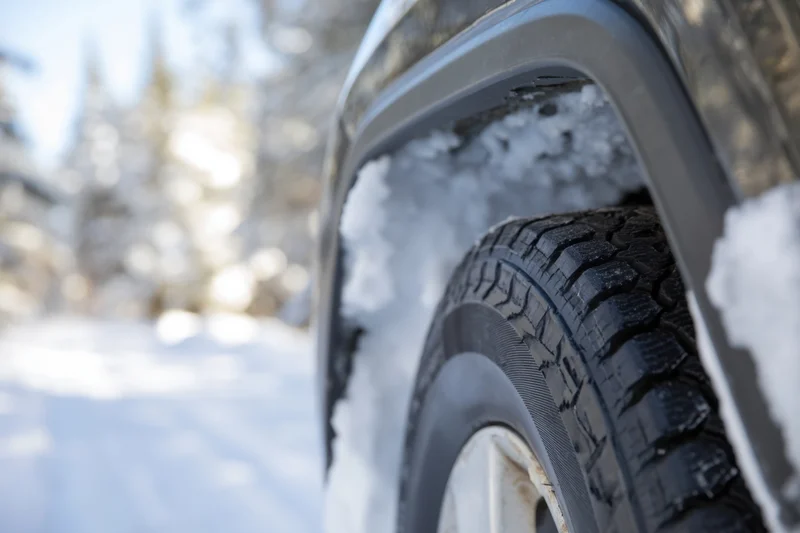 Closeup of black suv rear tire with snow in tread and fender, outdoors in snowy forest landscape
