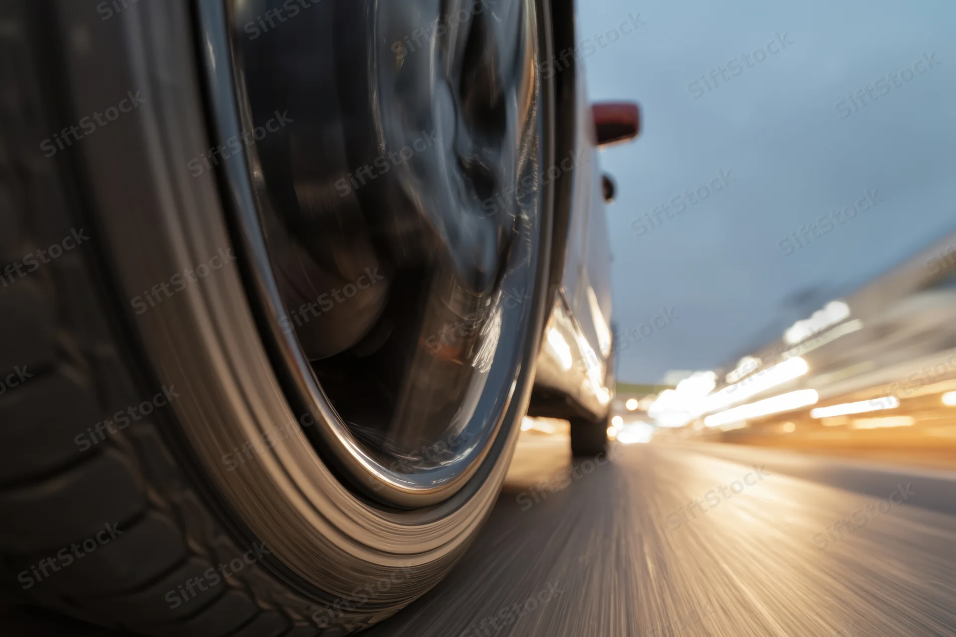 Close-up of a spinning car tire on a blurred highway at night with city lights streaking in the background