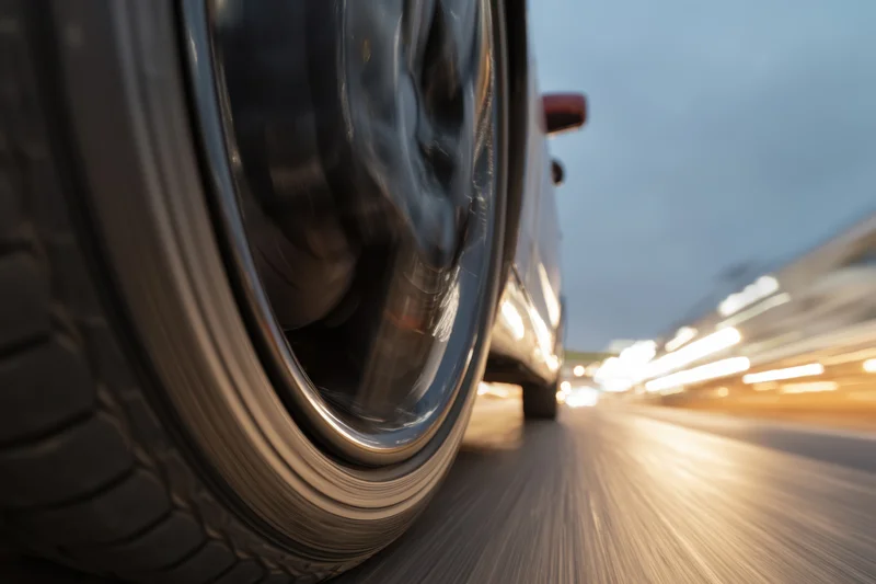 Close-up of a spinning car tire on a blurred highway at night with city lights streaking in the background