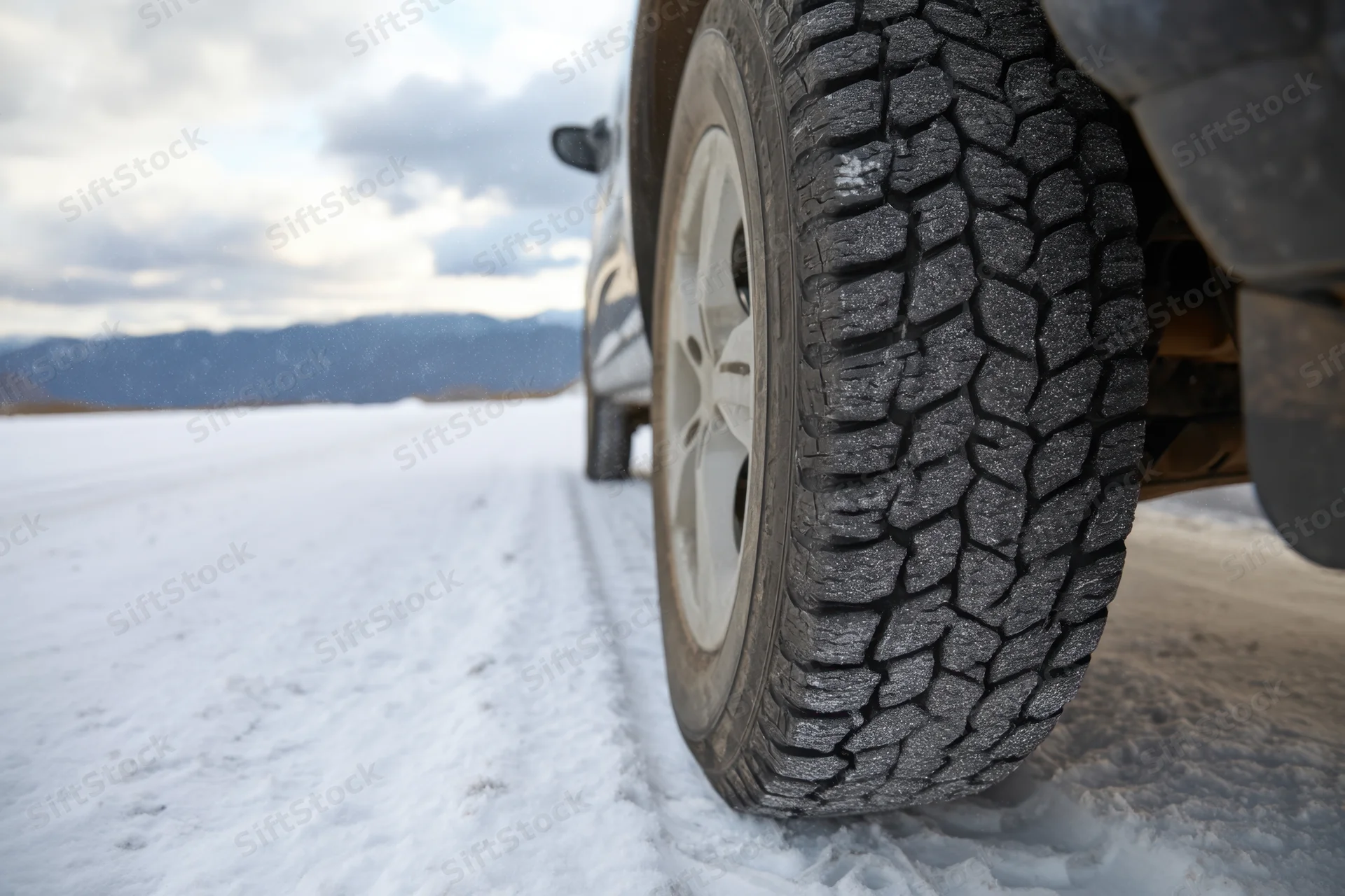 Close-up of a vehicle tire with deep tread on a snow-covered road near mountains