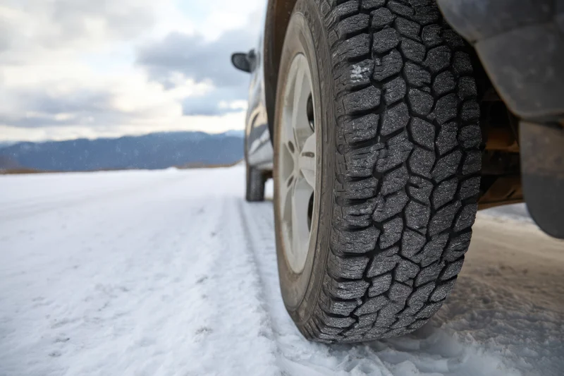Close-up of a vehicle tire with deep tread on a snow-covered road near mountains