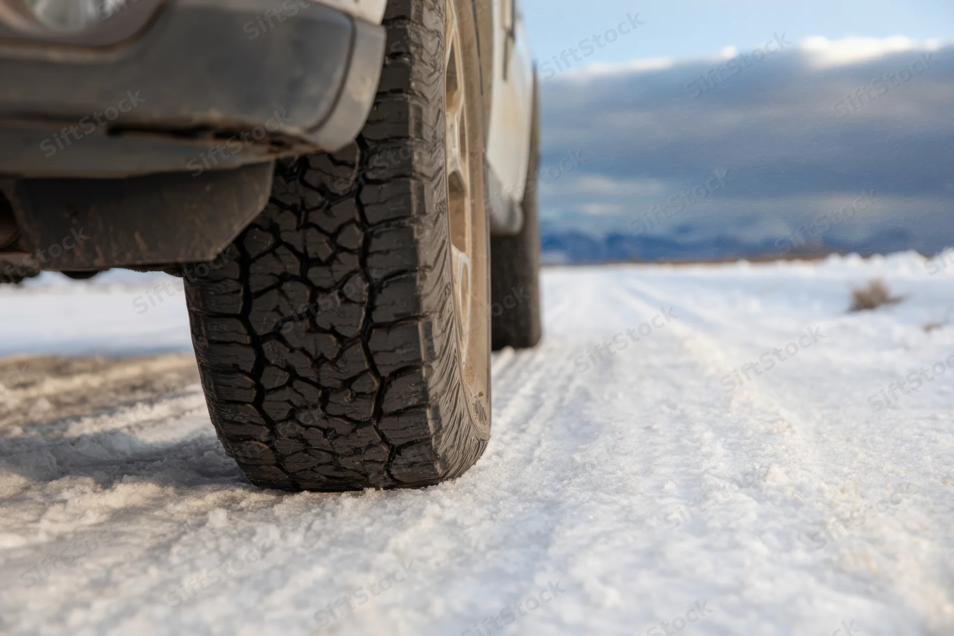 Close-up of a vehicle tire with deep tread on a snow-covered road in a mountainous winter landscape
