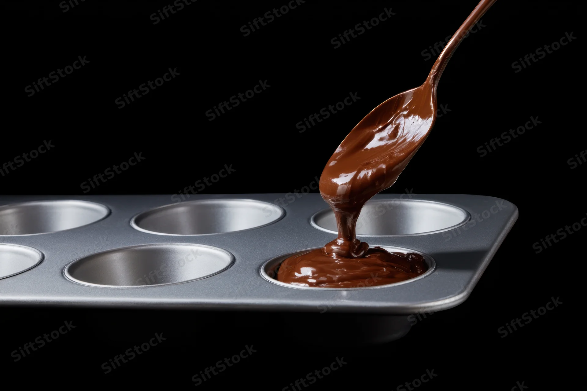 Molten chocolate being poured from a spoon into a muffin tin mold