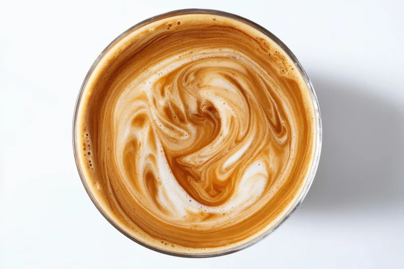 Creamy coffee surface with swirling foam pattern in a glass cup viewed from above