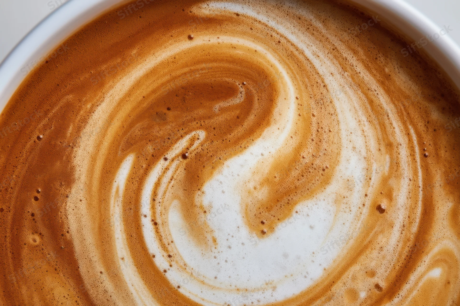 Creamy coffee surface with swirling milk foam pattern in a cup