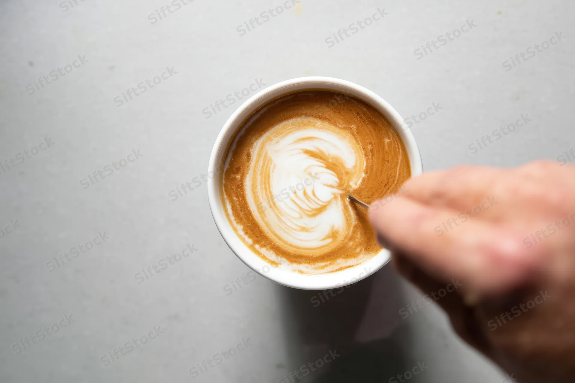 Hand drawing a heart-shaped latte art design in a cup of coffee on a gray surface