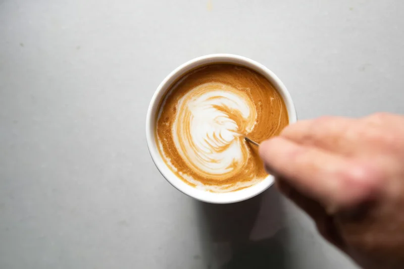Hand drawing a heart-shaped latte art design in a cup of coffee on a gray surface