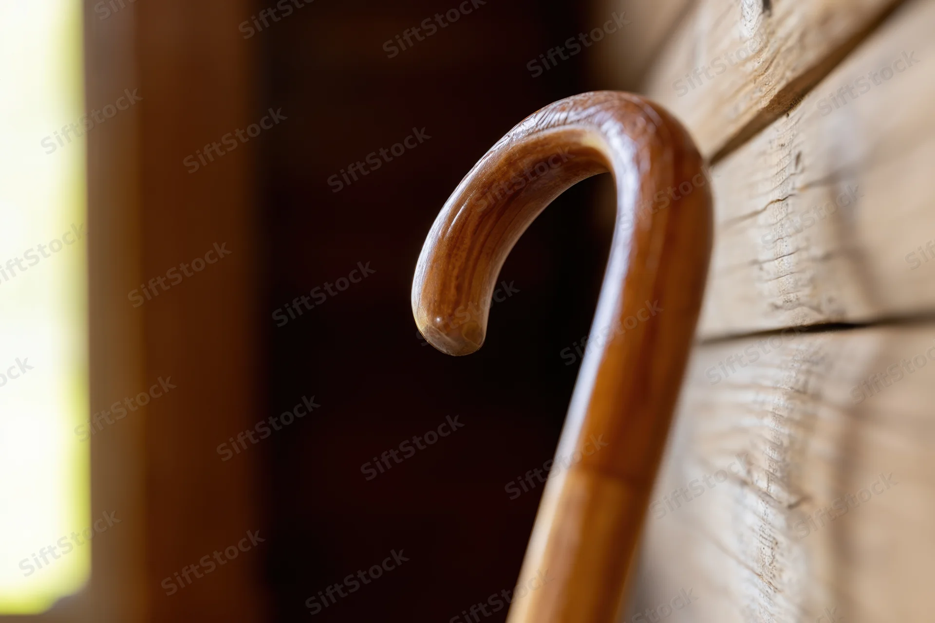 Curved wooden cane handle leaning against a rustic log wall