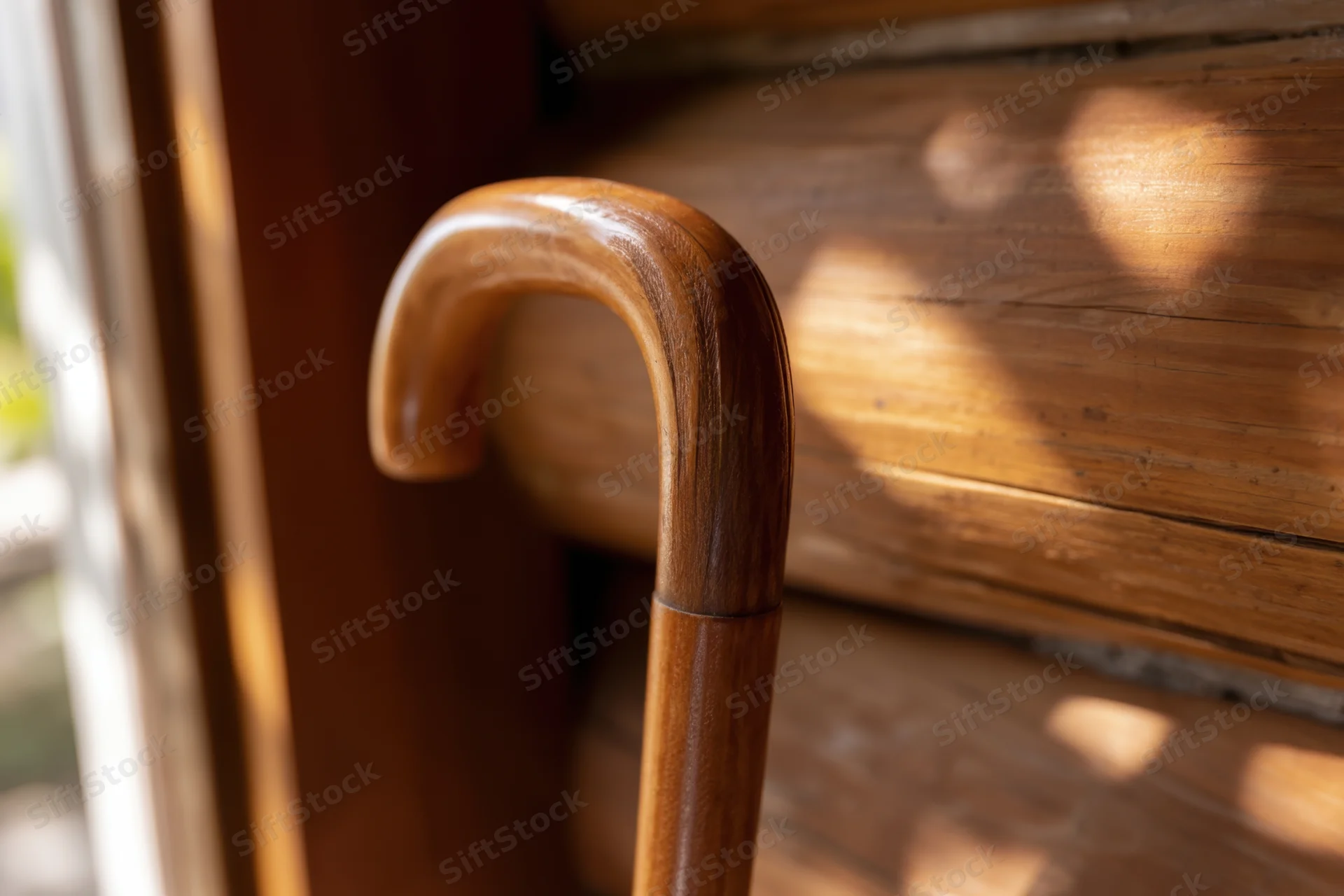 Wooden cane with curved handle leaning against a wooden surface in a sunlit interior