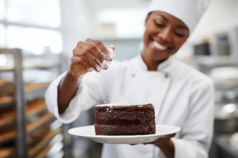 Female pastry chef sprinkling powdered sugar on chocolate cake in kitchen